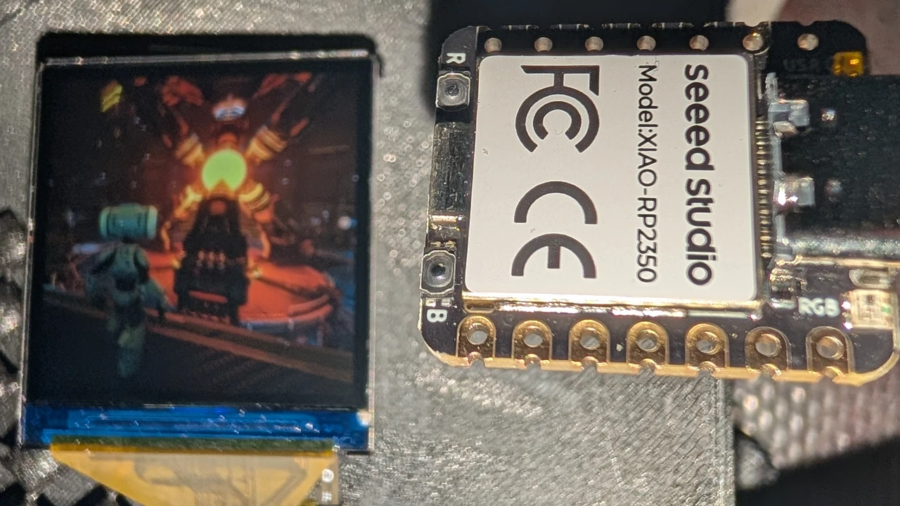 The small square prototype screen showing a robot in a reactor room, next to a XIAO RP2350 board of about the same size